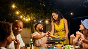 5ff5fbd1a478-family-and-friends-dining-at-an-outdoor-table-under-string-lights-by-the-pool-ev