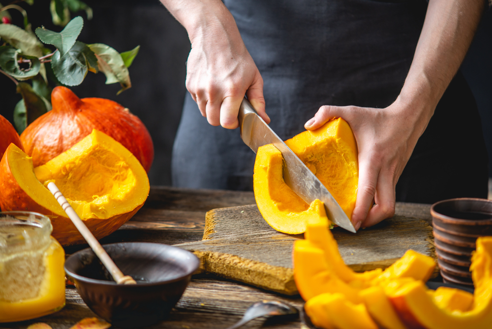 A,Woman,Cook,Cuts,An,Orange,Pumpkin,With,A,Knife